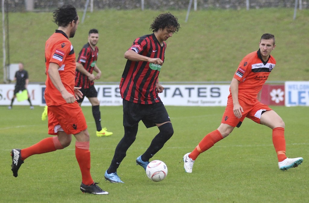 A midfielder in red and black runs at two defenders