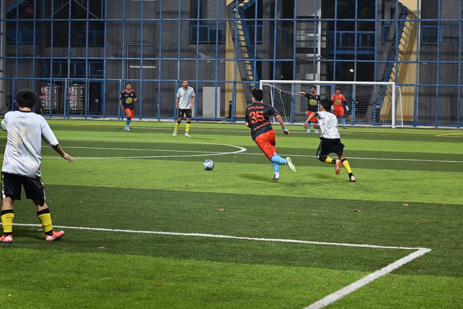 Players sprint for the ball on a floodlit small-sided pitch at night